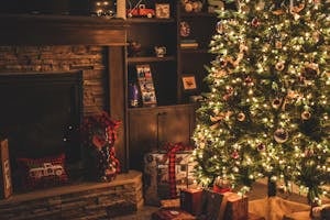Warm holiday scene of a decorated Christmas tree with gifts by a cozy fireplace.